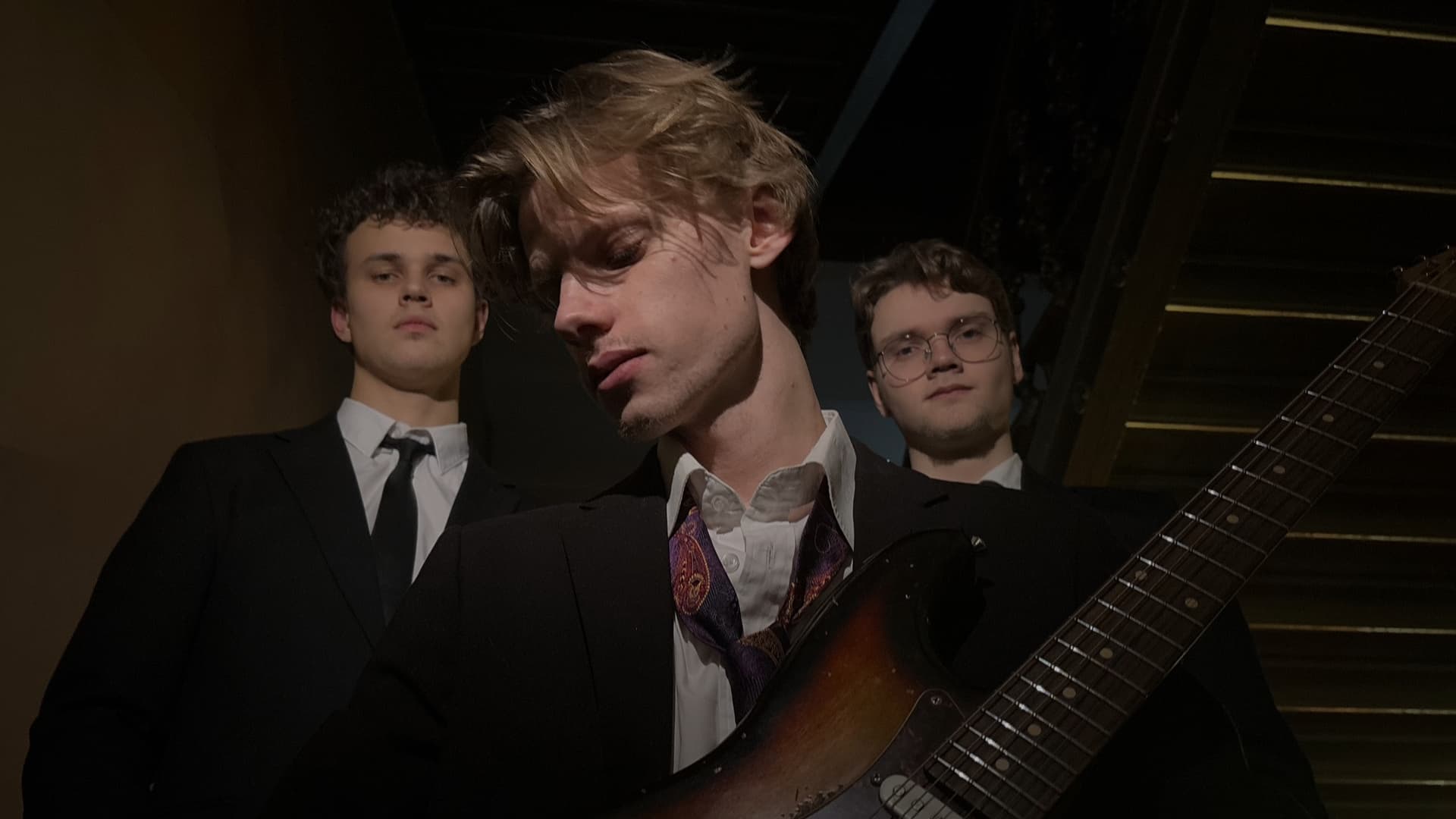 Anton Hultquist Trio in a dark stairwell, with guitar and suit.