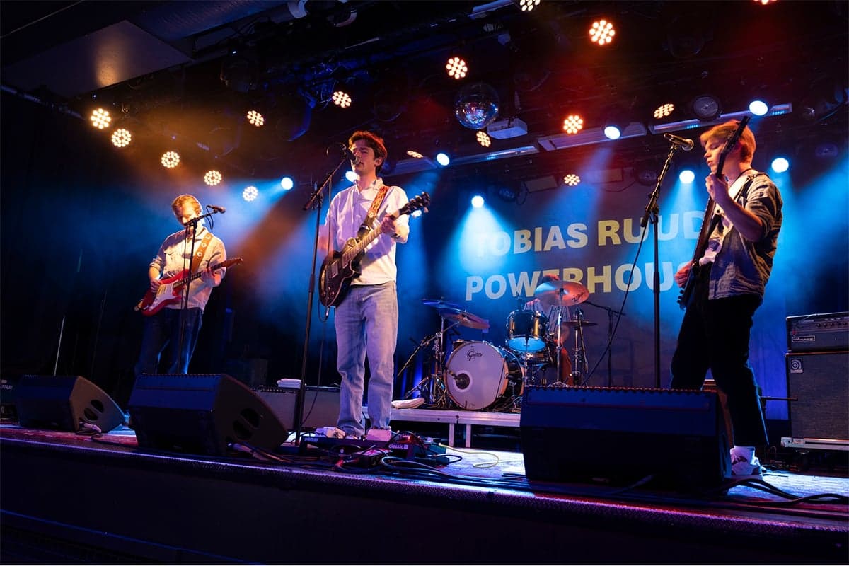 Tobias Ruud Powerhouse på scenen i blått og oransje lys, med bandnavnet på et banner bak trommeslageren.